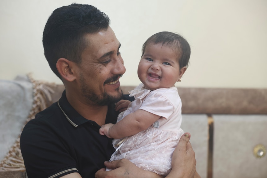 A smiling man holds a smiling 6-month-old baby