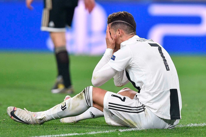 A soccer player sits with his head in his hands after a Champions League loss.