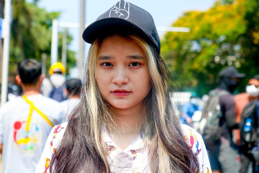 A woman with blonde and brown hair wears a cap with a fist on it as she stares at the camera.