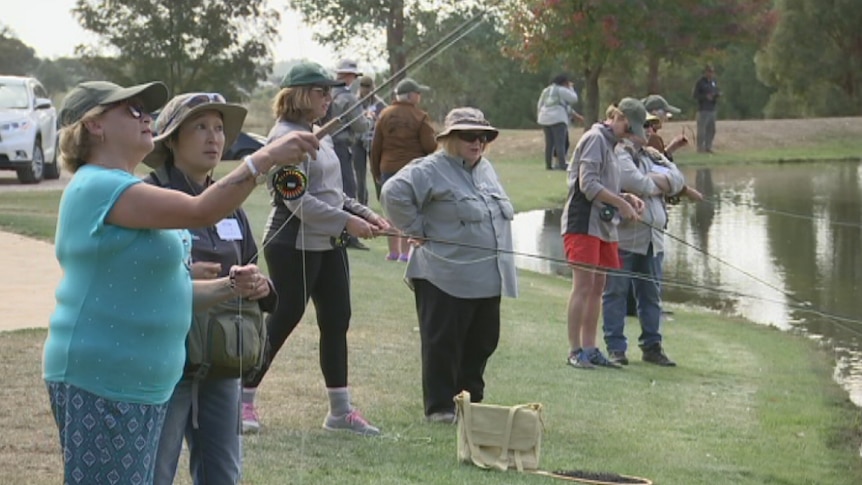 Women fly fish by a dam.