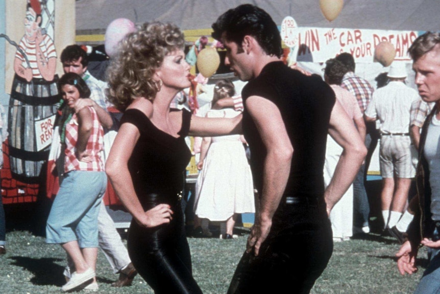 Olivia Newton-John and John Travolta dancing in a scene from Grease. Both are wearing black.