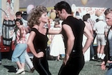 Olivia Newton-John and John Travolta dancing in a scene from Grease. Both are wearing black.