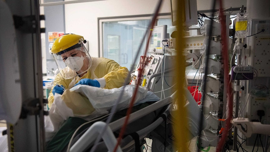 A nurse in PPE works with a patient inside the Intensive Care Unit