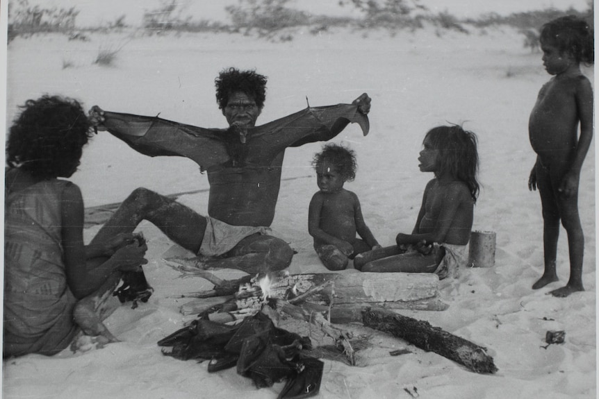 An Indigneous man spanning the wings of a bat with a woman and three children watching.