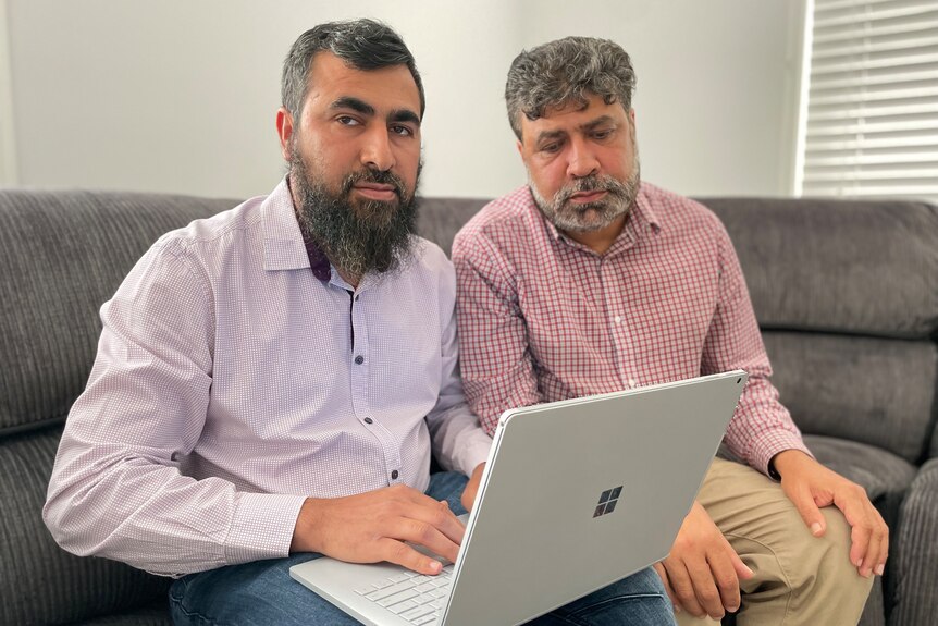 Two Afghan immigrant brothers sitting on their couch one has is using a laptop