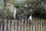 A house visible through trees and behind a picket fence