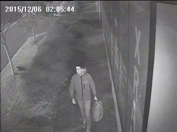 Black and white CCTV footage of a man walking down the street.