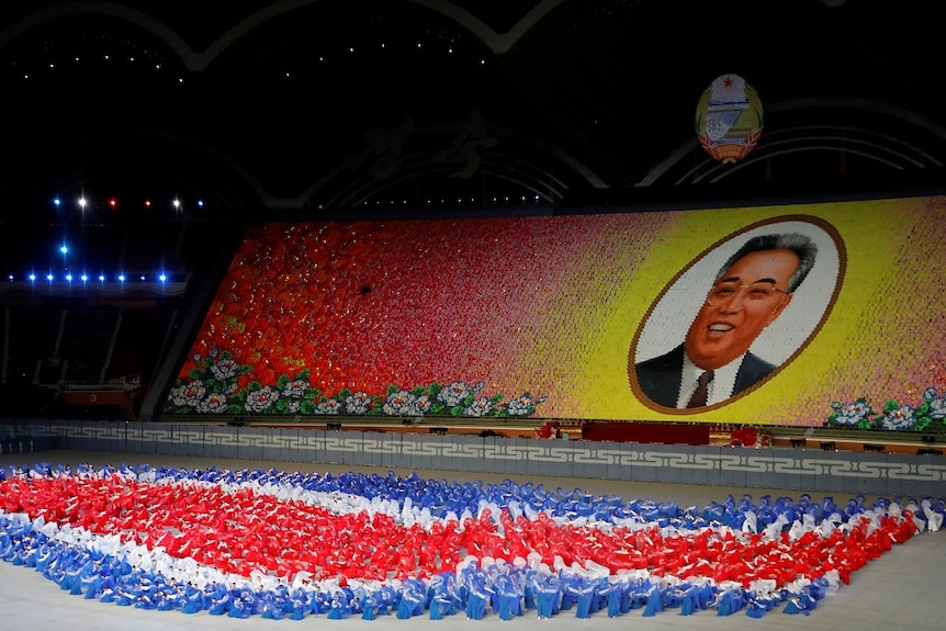 Thousand of performers in a stadium use coloured cards to form a cartoonish portrait of Kim Il-sung.
