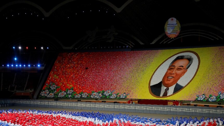 Thousand of performers in a stadium use coloured cards to form a cartoonish portrait of Kim Il-sung.