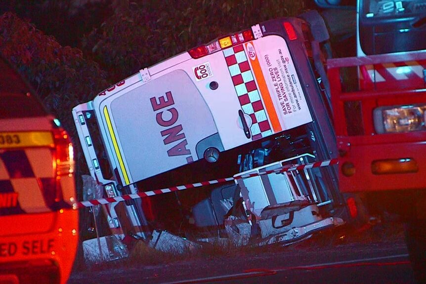 An ambulance can be seen tipped over at the side of the road, its contents spilled on the floor.
