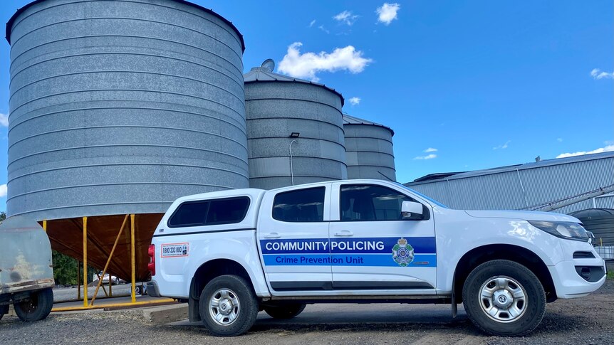 A Queensland Police car parked in front of grey metal silos on a farm.