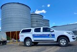 A Queensland Police car parked in front of grey metal silos on a farm.