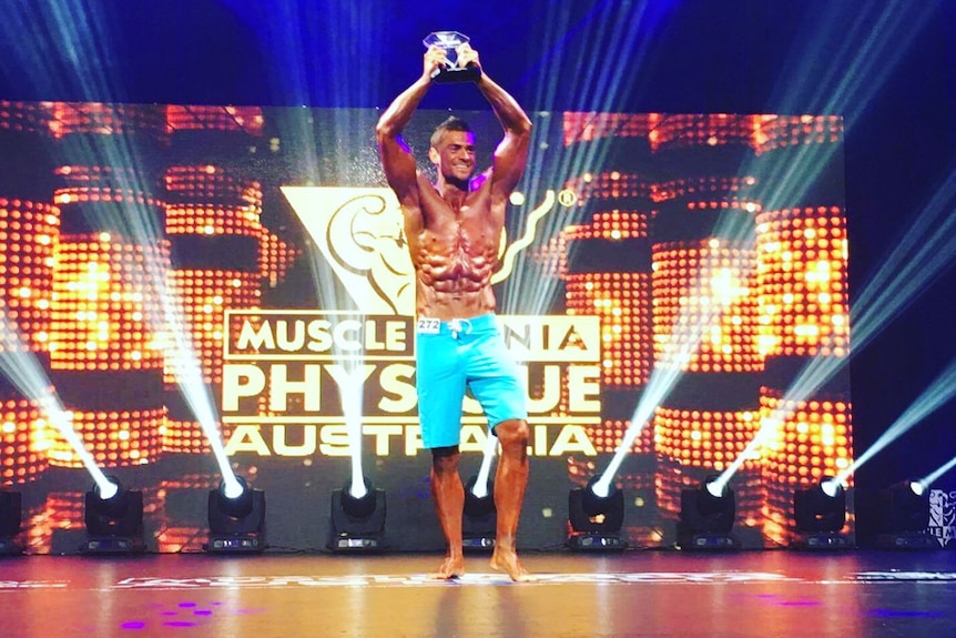 Lee Nagorcka holds bodybuilding trophy in the air