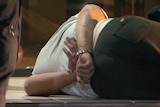 Man with trackpants and white shirt on with handcuffs lying down