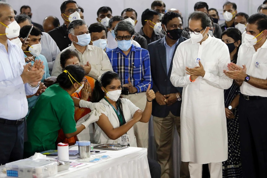 Indian health worker gives thumb up after receiving a vaccines surrounded by other health workers