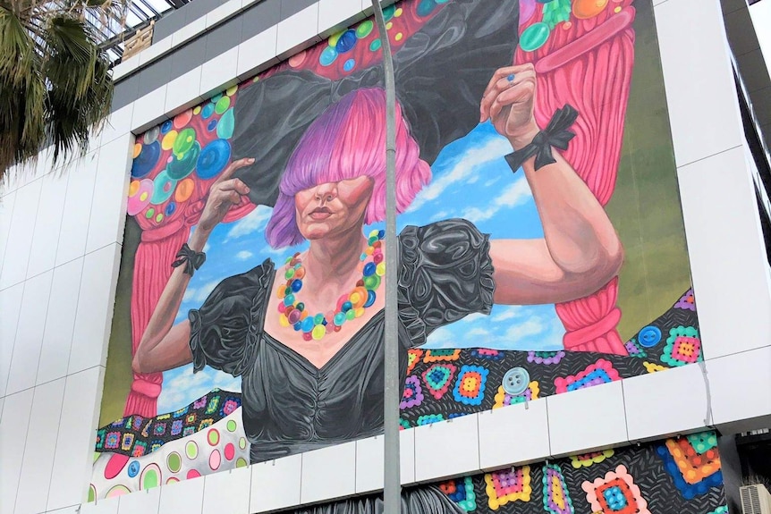 A mural of a woman with pink and purple hair painted on a wall