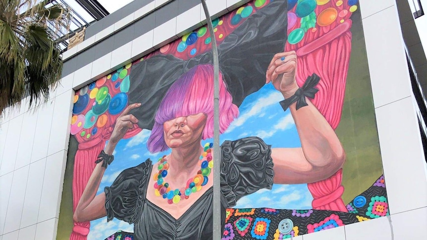 A mural of a woman with pink and purple hair painted on a wall