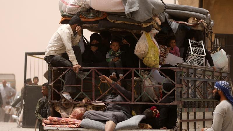 Men, women and children overcrowded in the back of a truck, packed in with their belongings