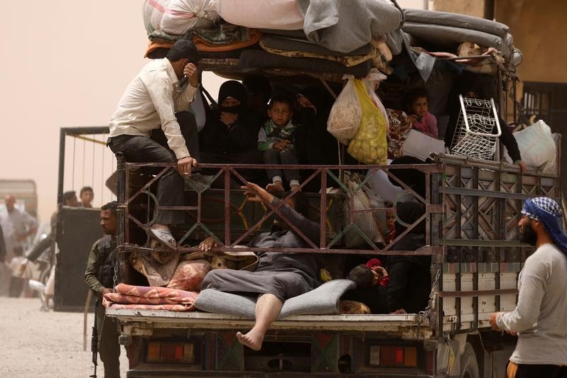 Men, women and children overcrowded in the back of a truck, packed in with their belongings