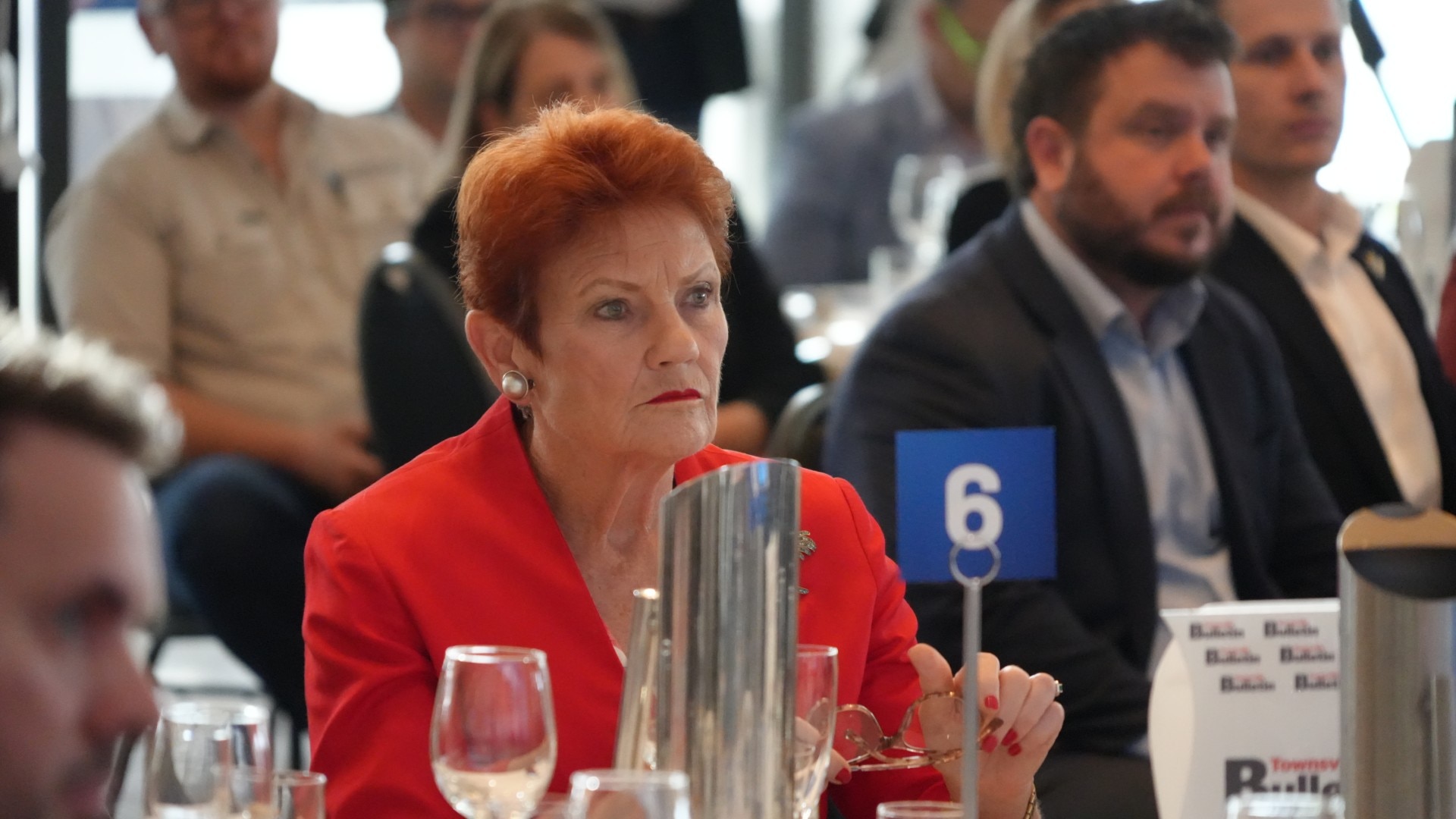 A woman sits at a table in the crowd of a function.