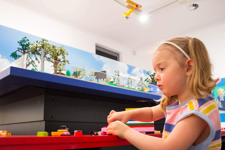 A girl playing with lego in front of a larger lego model