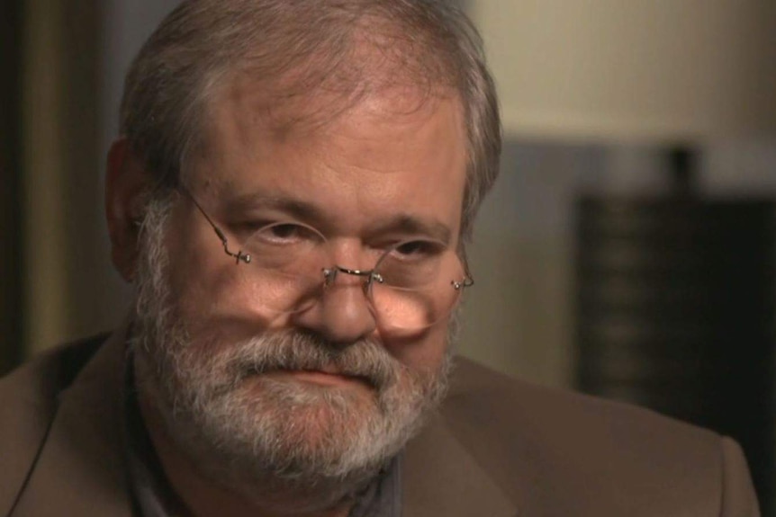 A man with grey hair and glasses looks forward