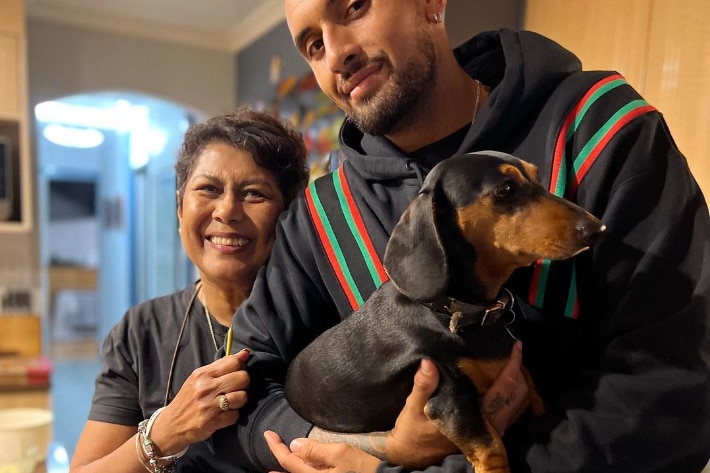 Nick holds a dog and stands next to his mother, they both smile.