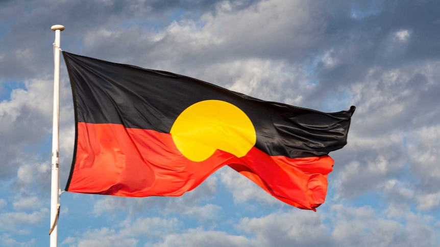 Australian Aboriginal Flag flies, grey clouds in background.