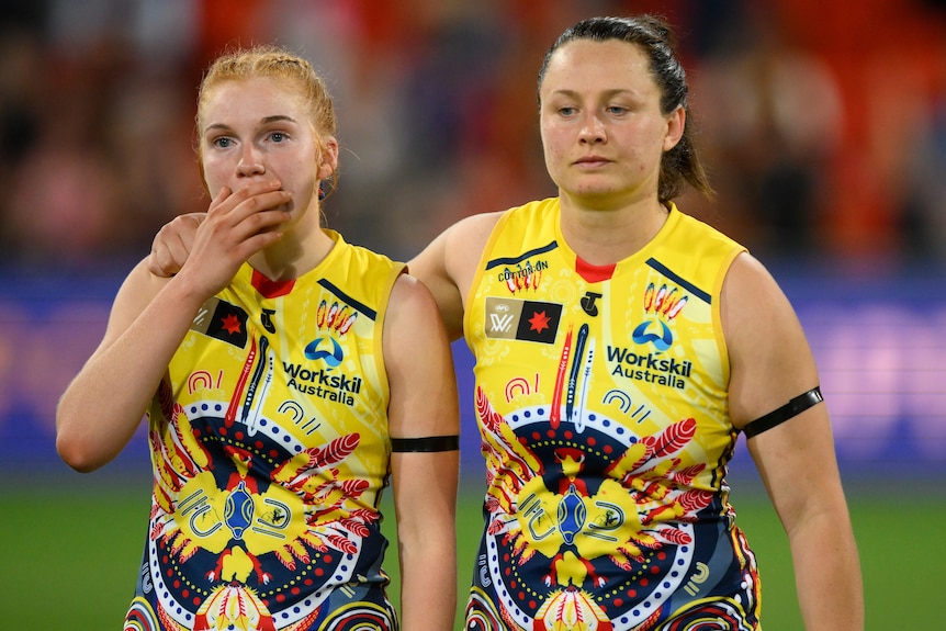 Two Adelaide Crows' AFLW players console each other after a loss to the Brisbane Lions.