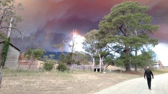 Fire flares in hills with farm building in the foreground in East Gippsland