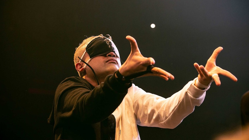 A blindfolded vogue performer raises two arms in front of him on stage at Sissy Ball 2019.