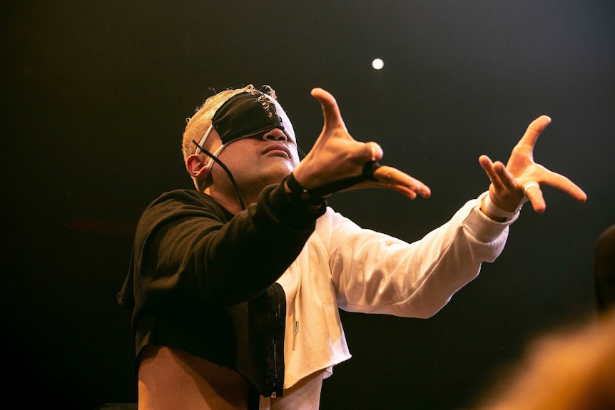 A blindfolded vogue performer raises two arms in front of him on stage at Sissy Ball 2019.