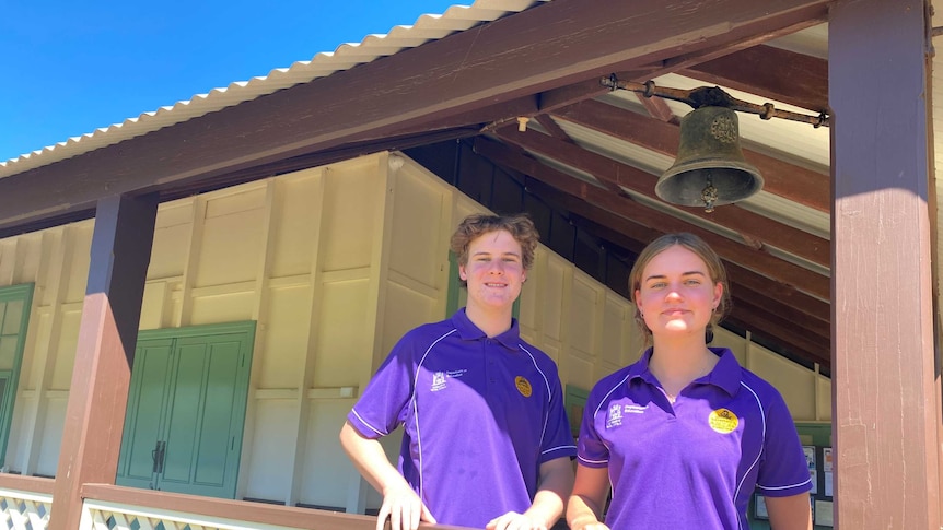 Two students in purple shirts stand on an old veranda