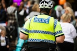 A photo of the back of a police officer wearing a high vis vest and bike helmet.