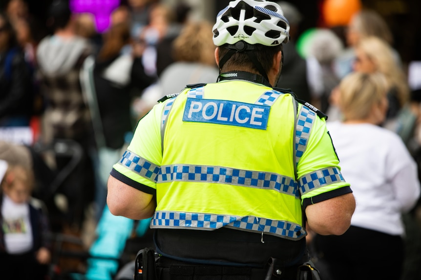 A photo of the back of a police officer wearing a high vis vest and bike helmet.