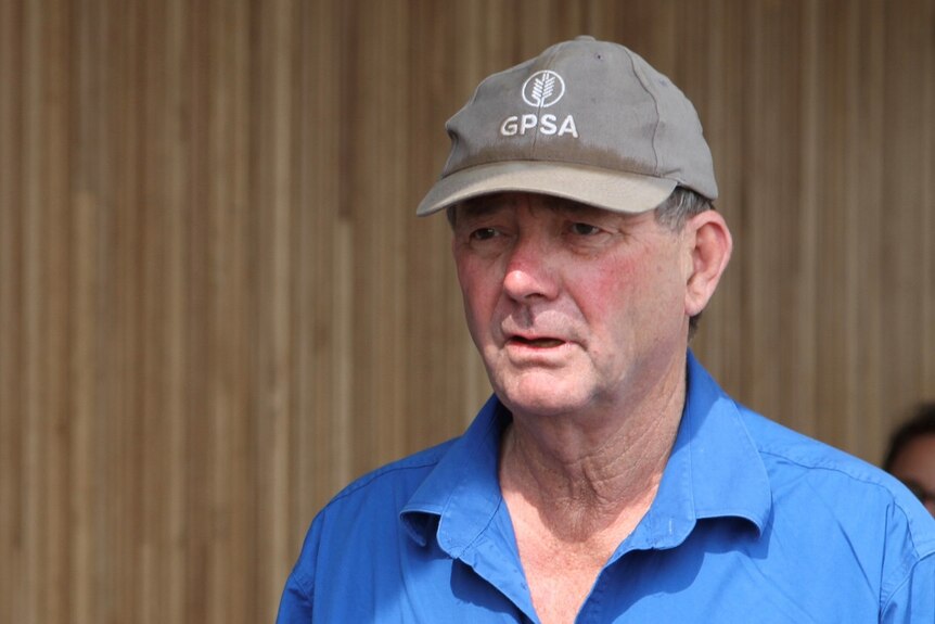 A man in a blue shirt and black hat looks off-camera with a serious expression on his face.