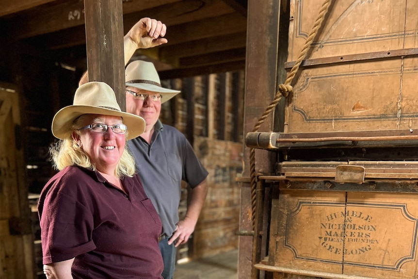 A man and woman inside an historic woolshed wearing hats and country clothing
