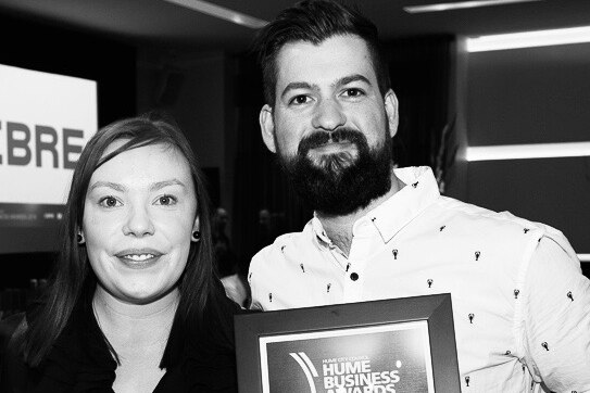 A black and white photo of a woman and man holding an award smiling at the camera