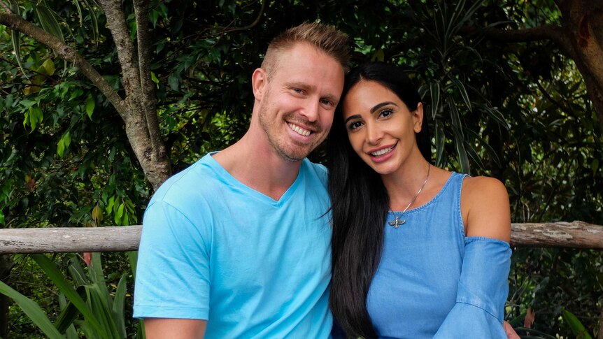 Couple Nathan Secomb and Auzita Pourshasb sitting in front of leafy background.