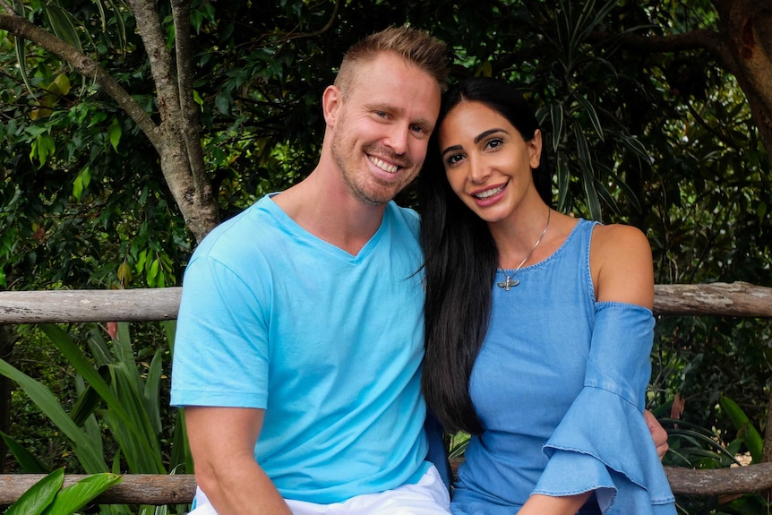 Couple Nathan Secomb and Auzita Pourshasb sitting in front of leafy background.