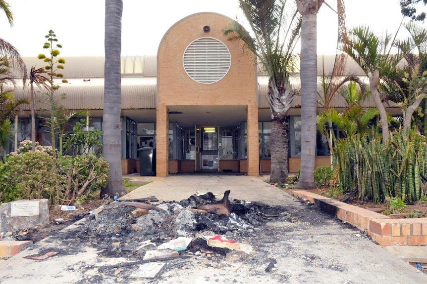 A pile of burnt debris lies on the ground outside the main entrance to a prison.