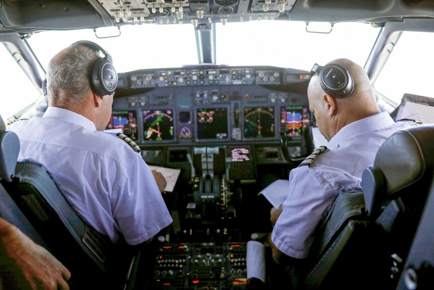 Two men in pilot's uniforms sitting in the cockpit of a passenger plane