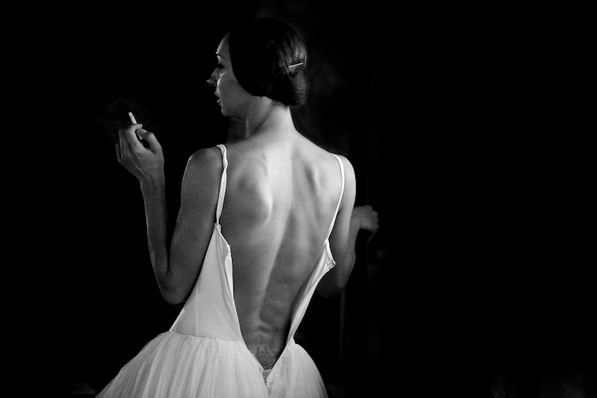 A ballet dancer stands with cigarette in hand with her costume unzipped