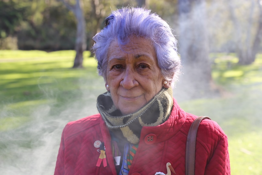 An older woman outside on a cold day with smoke billowing behind her.