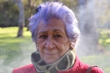 An older woman outside on a cold day with smoke billowing behind her.
