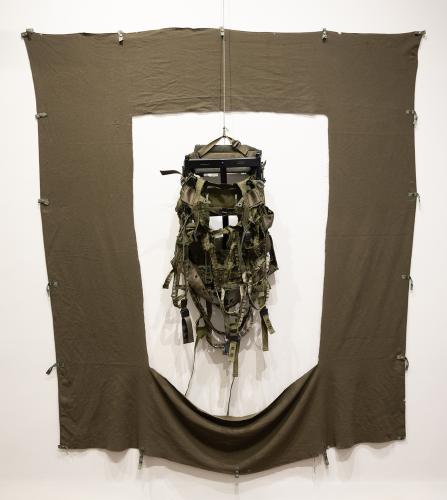 An army backpack hanging on a wall in a gallery
