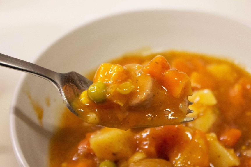 Carrots, sausage, peas and potato in gravy from a tin on a fork, showing ready-meals as a hack in the meal prep process.