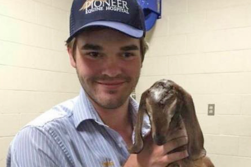 Man in blue cap and shirt holding a goat