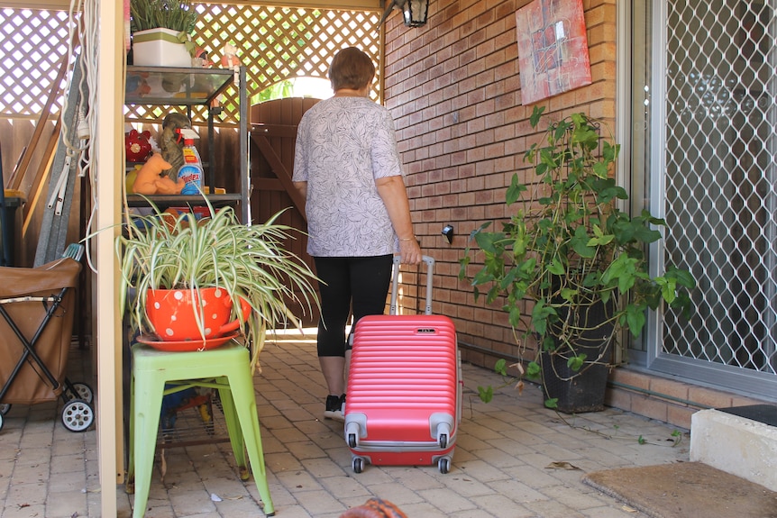 woman from the back, leaving a courtyard with pink suitcase