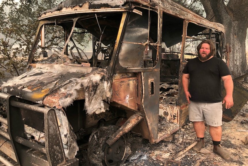 A man stands amid the rubble of a bushfire-hit property